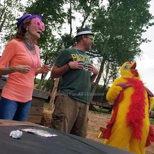 Man and Woman with Birthday Hat and Glasses Clucking Next to Chicken Costume
